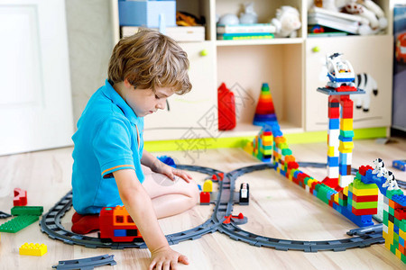 可爱的金发小男孩玩五颜六色的塑料积木和创建火车站孩子在家图片
