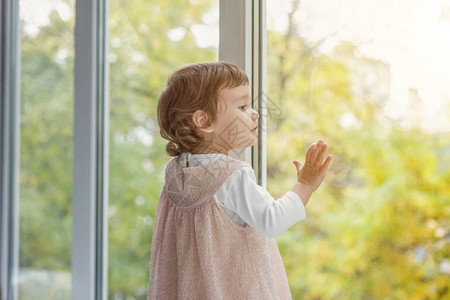 穿着柔和粉色连衣裙的可爱甜美微笑小女孩站在家里明亮的客厅窗台上微笑着童年学前青图片