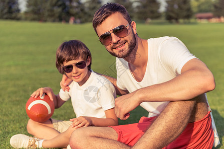 可爱的小男孩和他戴着太阳镜的英俊年轻爸拿着一个球图片