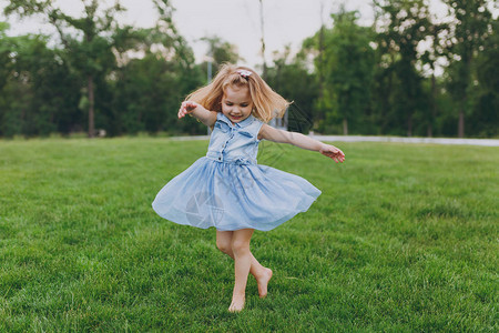 相当可爱的小女孩穿着牛仔裙在公园的绿草坪上转圈图片
