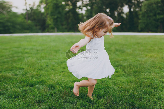 漂亮可爱的小宝贝女孩穿着轻便的衣服在公园的绿草坪上转圈图片