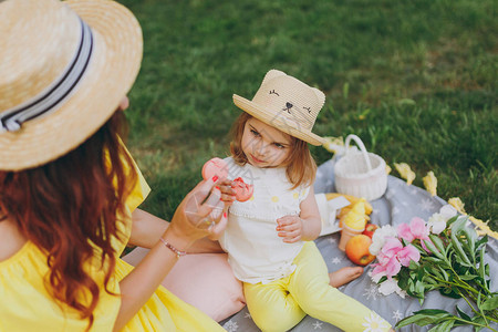 穿着黄色衣服的女人在公园的绿草坪上休息玩得开心和小女孩一起吃杏仁甜点图片