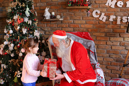 华丽的女孩非常高兴地向坐在大而柔软的扶手椅上的圣诞老人送礼盒圣诞惊喜图片