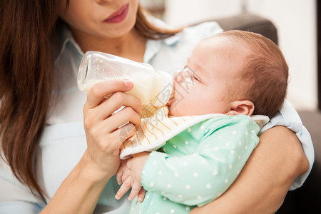 一个可爱的新生婴儿紧关地喝着瓶装牛奶而图片