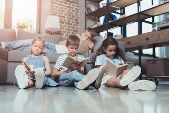 集中的多文化儿童群体在家中一起阅读书本图片