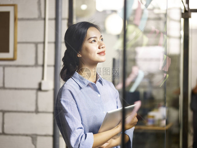 年轻女商人看着玻璃墙上的粘贴笔记图片