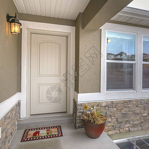一个家的方形白色前门和反光窗与道路和多云的天空相映成趣彩色门垫盆栽植物和壁灯装饰着图片