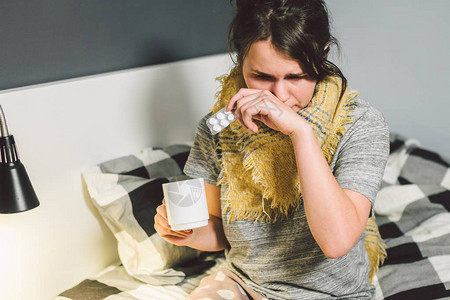 年轻美丽的高加索女人在床上患感冒流感高烧和高温女孩用一杯水服用图片