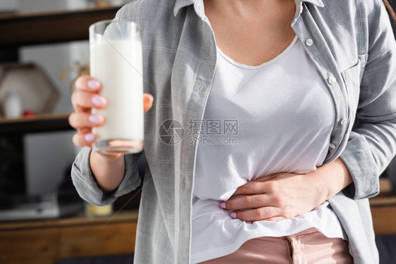 乳糖不耐症妇女在触摸胃部时拿着一杯牛奶的剪影图片