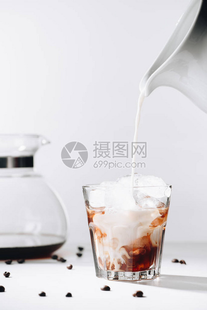 将牛奶倒入冷酿咖啡工艺咖啡机和灰底烤咖啡豆的杯中图片