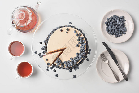 玻璃摊子上有茶和餐具的蓝莓片芝士蛋糕上图片