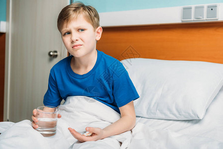 医院病床和住院病人护理概念中不满意的男孩用杯水和药品装在医院床图片