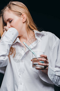 身穿男子衬衫的年轻女子打哈和拿着杯水用牙刷在黑色背景上图片