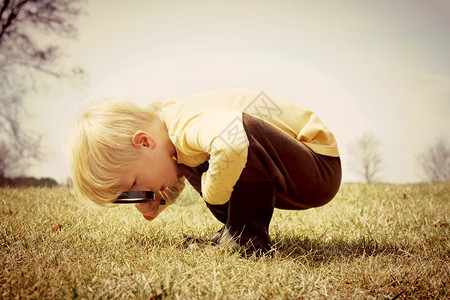 一个小孩弯下腰看着草地用放大镜来调查一些东西图片