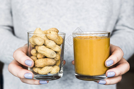 女人手里拿着两个罐子带壳的花生和花生酱素食和图片