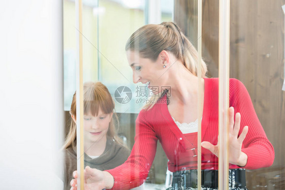 带着她女儿的开心女人在卫生用品店展厅的一个淋浴间里看一个洗澡房图片