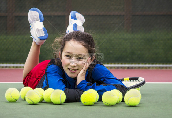 微笑的少女网球运动员躺在一排网球后面的水平肖像图片
