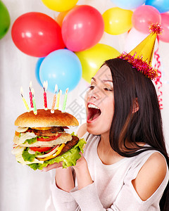 生日那天戴着派对帽吃汉堡的女人图片
