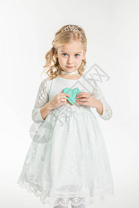 可爱的小女孩拿着心形曲奇饼干看着在白色上背景图片