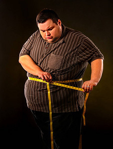男人腹部脂肪与卷尺体重减轻在黑色背景上的身体周围节食第一图片