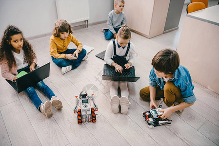 儿童在干教育班坐在地板上时编程机器人的高图片