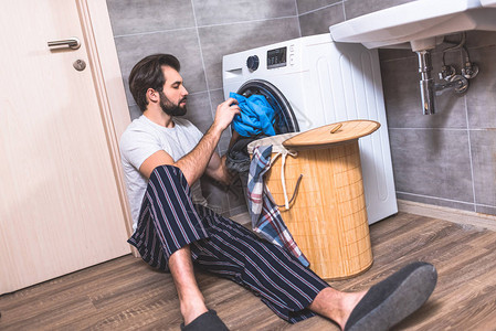 英俊的孤独者把衣服放在浴室的洗衣机里图片