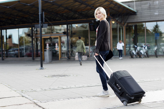 坐在火车终点站的年轻女士带着一个轮式手提箱走来去图片
