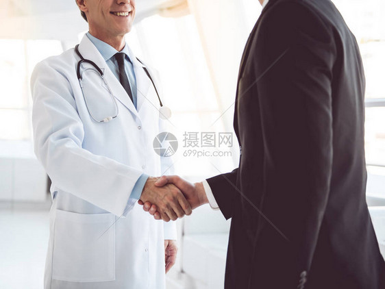 长得英俊成熟的医生和青年商人站在医院大厅时握手的剪裁图片