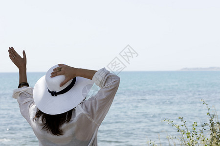 女孩在地中海前挥舞着高盘的白帽子手挥图片