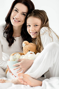 可爱的女儿和母亲坐在床上家里有棉花糖浆图片
