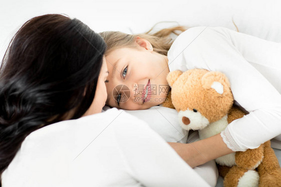 有泰迪熊的可爱女儿和妈在床上放松在图片