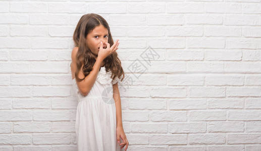 年轻的西班牙裔孩子在白色的砖墙上闻到一些臭味和恶心的东西图片