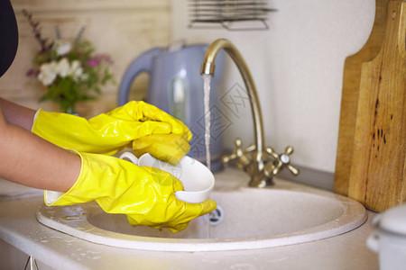紧握着身戴黄色手套在厨房洗盘子的妇图片