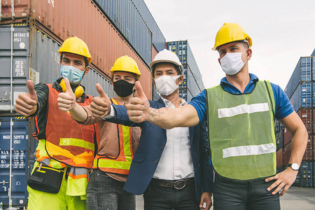 建筑工人团队正在仓库港口与身穿蓝色西装的商人竖起大拇指他们都戴着口罩戴着口图片