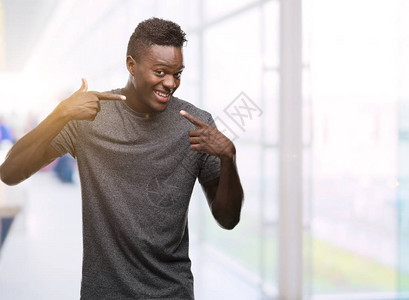 身穿灰色T恤的年轻非洲裔美国人微笑着自信地展示和用手指牙齿和嘴巴指点图片