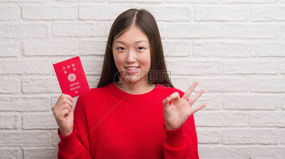 持有日本护照的青年女子在砖墙上翻墙图片