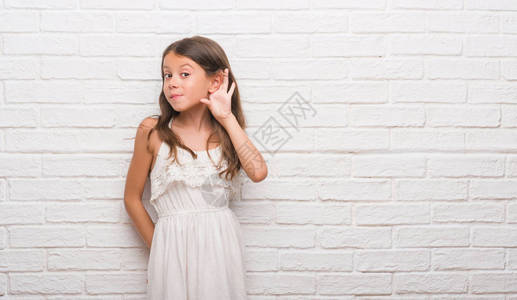 在白砖墙上哭着笑听谣言或八卦的年轻西班牙小孩耳聋的概念图片