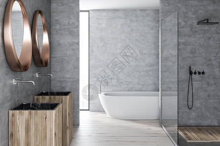 现代洗手间内部有混凝土墙木地板玻璃墙淋浴白浴缸和两面圆镜子的图片