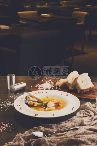 法国美食餐厅海鲜汤配白鱼虾和贻贝在盘子里撒上香料和热面包用亚麻布和勺子在木桌上新鲜烹图片