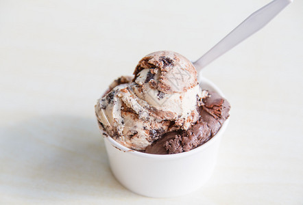 巧克力和饼干面饼冰淇淋在白柜子上用塑料勺子的图片