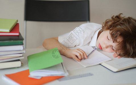 小学生坐在课桌前睡着了在桌子上的一摞书男孩手里拿着一支圆珠笔头在图片