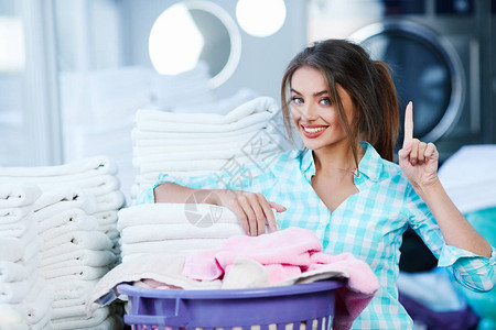 在洗衣房靠近玫瑰色和白色亚麻布的女人感觉亚麻布的柔软和洗涤的新鲜感女人微笑背景图片