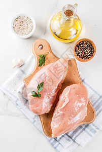 白色大理石背景上的生肉鸡胸肉橄榄油香草和香料图片
