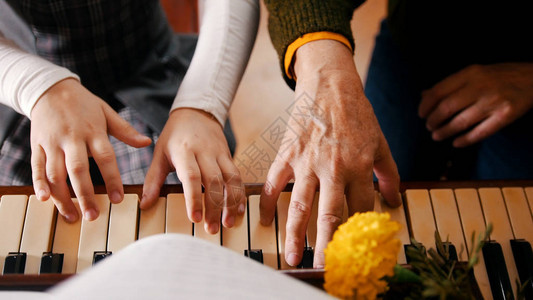 一个小女孩在音乐课上弹钢琴一位老师帮助她手举起图片