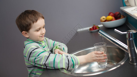 儿童7岁男孩将自来水倒入玻璃杯中图片