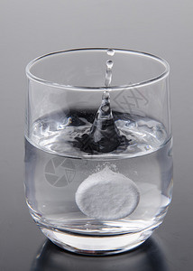 泡腾片落入灰色背景的一杯水中图片
