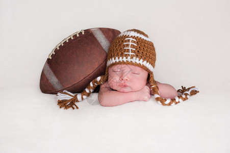 一个两周大熟睡的新生男婴的画像他与戴着钩编足球帽的图片
