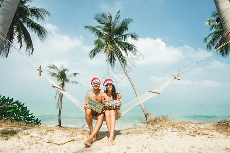 庆祝圣诞节和新年的轻美夫妇坐在棕榈树下海滩吊床上图片