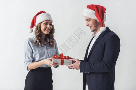穿着办公室服装的帅男和漂亮女孩圣诞老人帽子拿着一个礼物盒微笑着图片