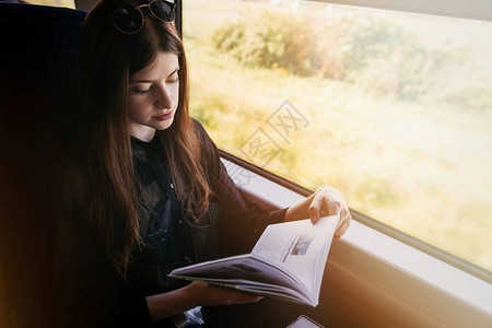时尚的时髦女孩在火车的窗户灯看书乘火车旅行的概念美丽的年轻女子拿着纸质书旅行和交背景图片